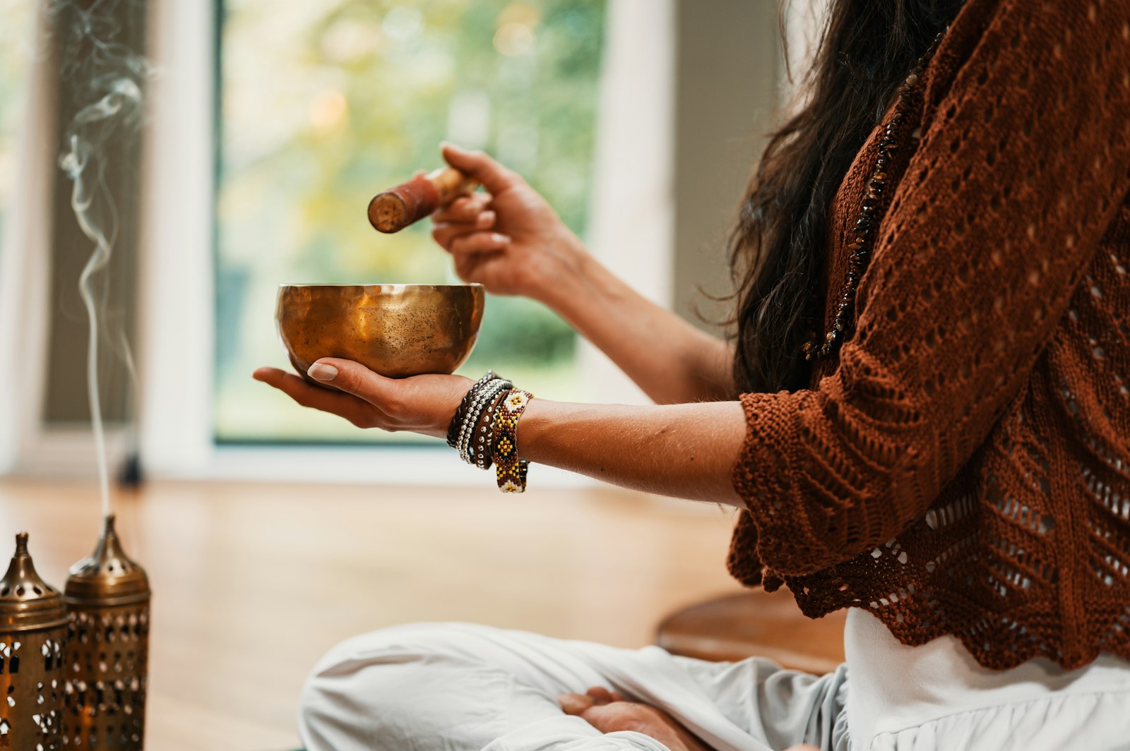 A person seated cross-legged holding a Tibetan singing bowl, incense smoke curling in soft light