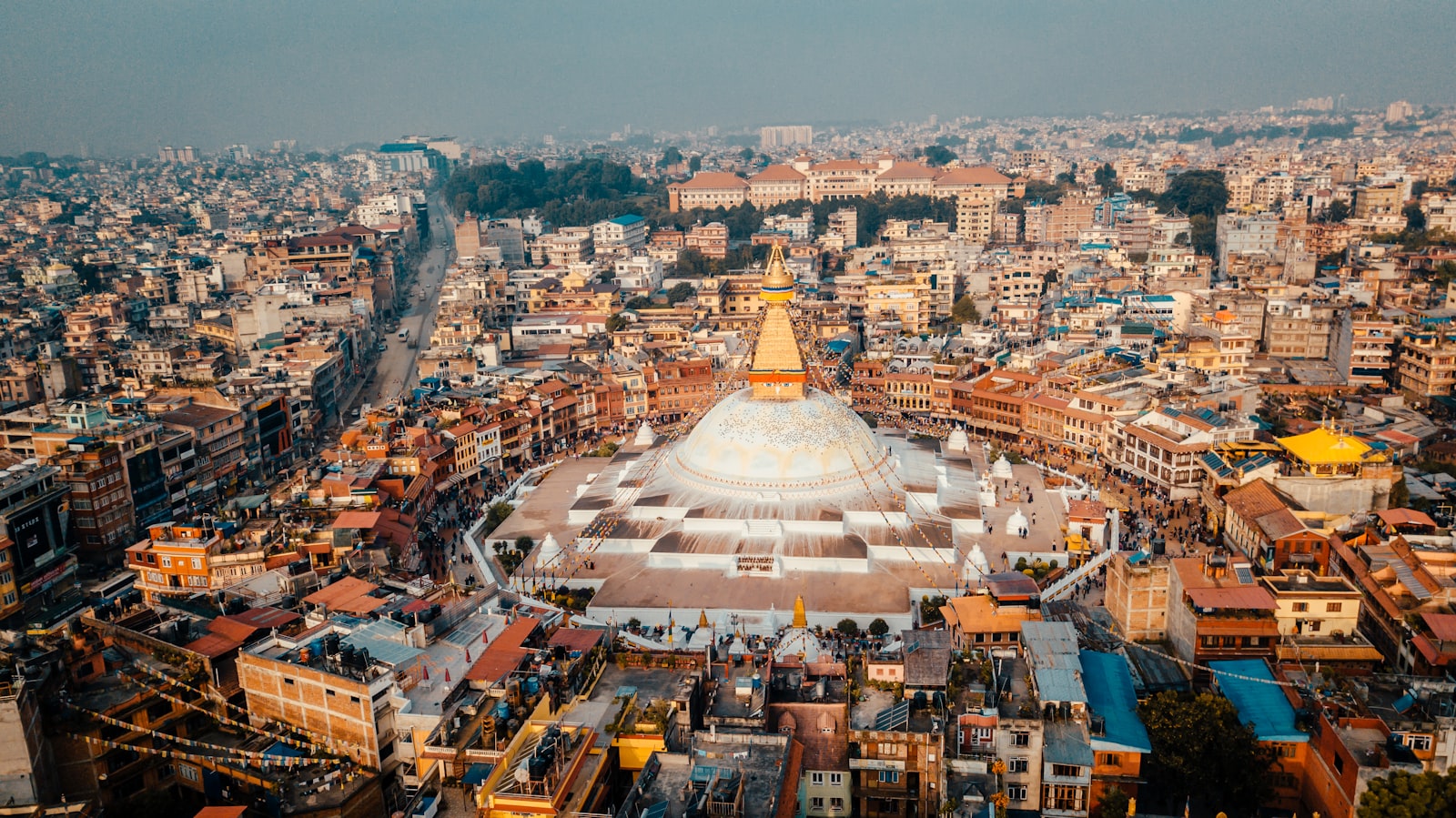 The golden-spired Boudhanath stupa at warm light, ringed by the rooftops of Kathmandu