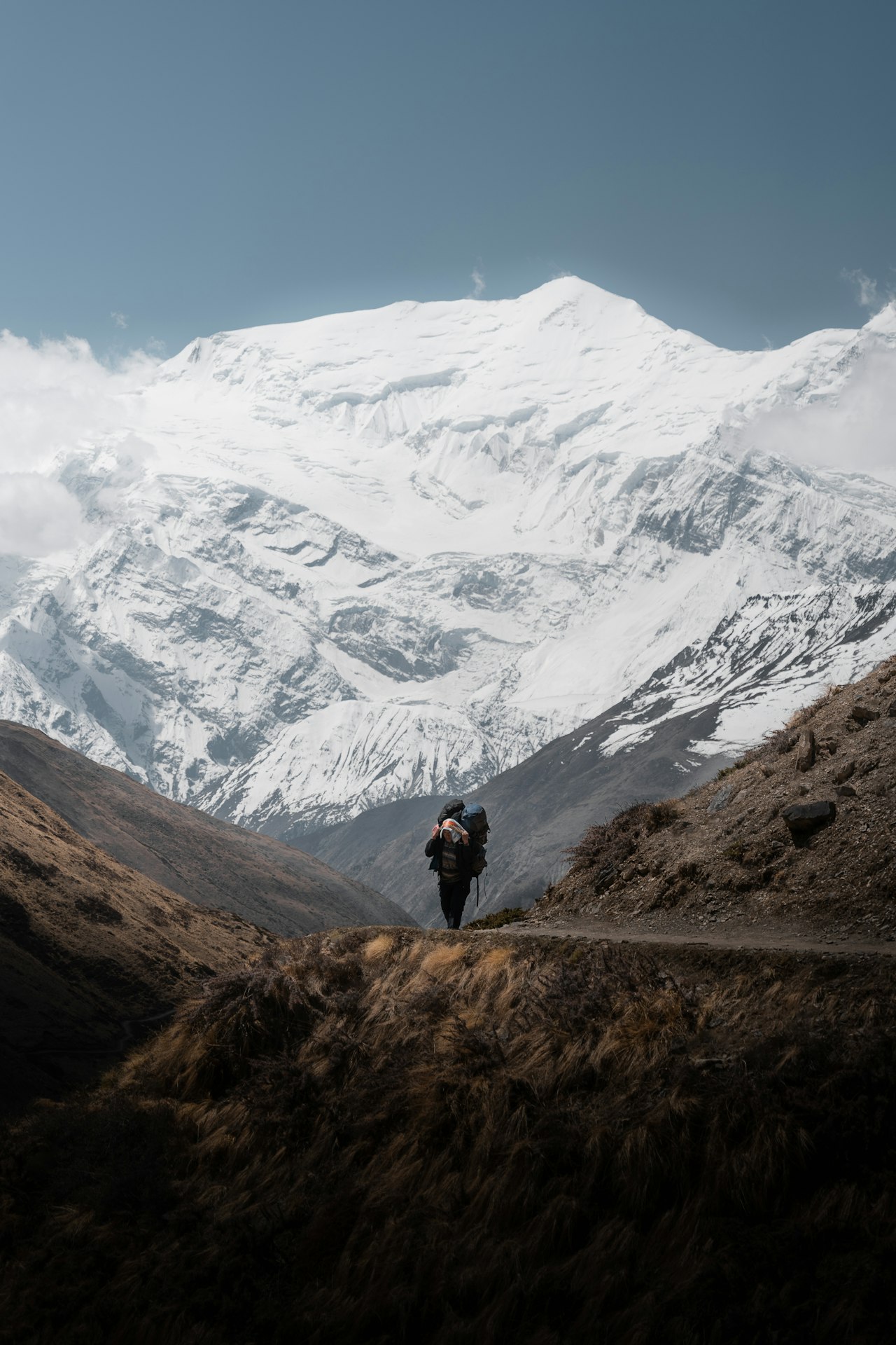 A solitary trekker on a remote Himalayan trail dwarfed by a vast snow-capped Annapurna peak in Nepal