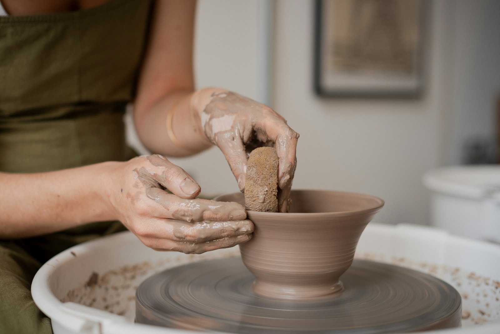 Hands centring and pulling up wet clay on a traditional potter's wheel